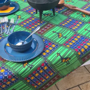 Authentic African-inspired colorful tablecloth with vibrant geometric patterns and animal motifs, set for outdoor dining with traditional bowls and utensils.