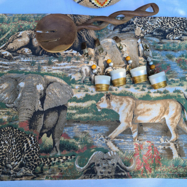 Decorative African wildlife-themed tablecloth with 4 paint-dipped tablecloth weights, featuring beaded accents, alongside a wooden serving spoon.