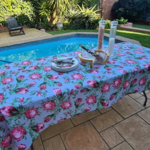 Handmade tablecloth with a vibrant protea flowers print, set on an outdoor table by a pool, surrounded by lush greenery, creating an elegant and inviting atmosphere for outdoor dining.