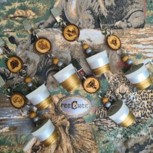 Six handcrafted concrete tablecloth weights, double-dipped in gold and silver, featuring laser-cut MDF disks with Big 5 animal designs and bead details. The weights are displayed on a leopard print fabric, with an African theme throughout.